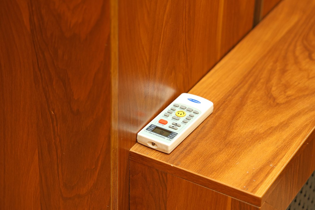 A white air conditioner remote with a yellow smiley face button on wood