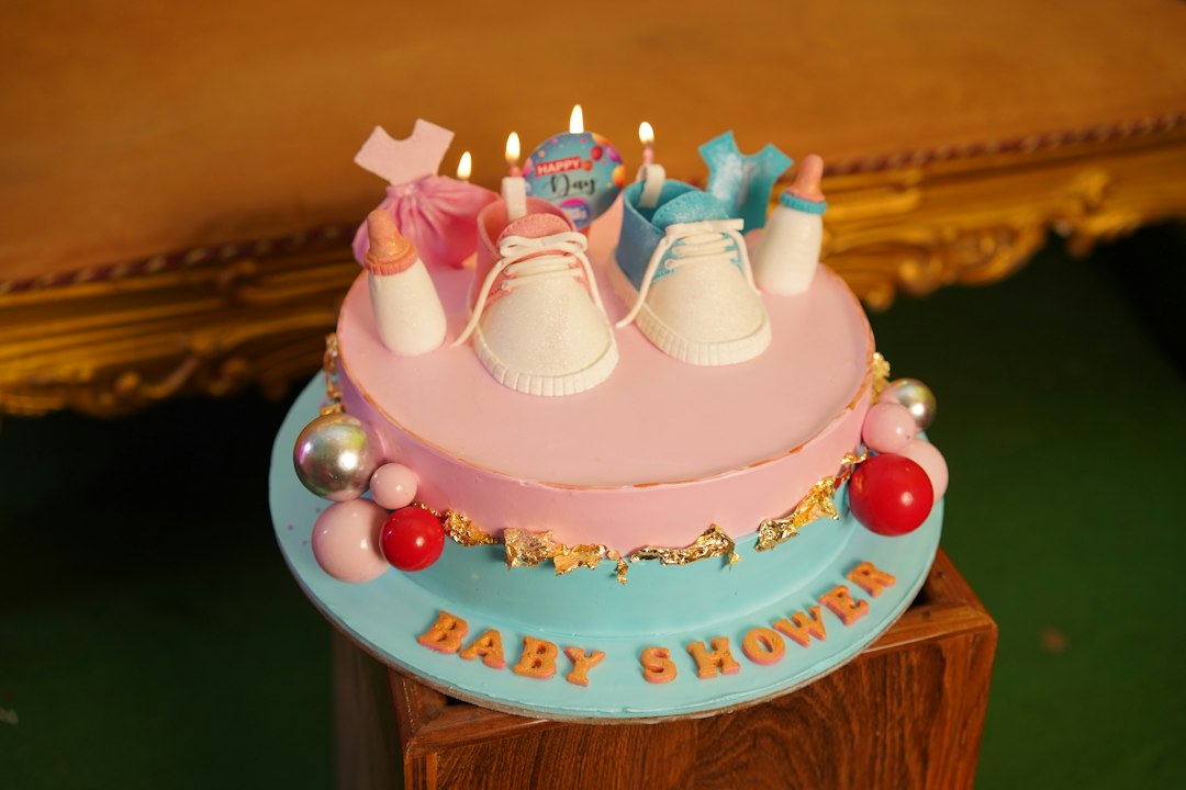 A baby shower cake with pink and blue frosting, baby shoes, and lit candles