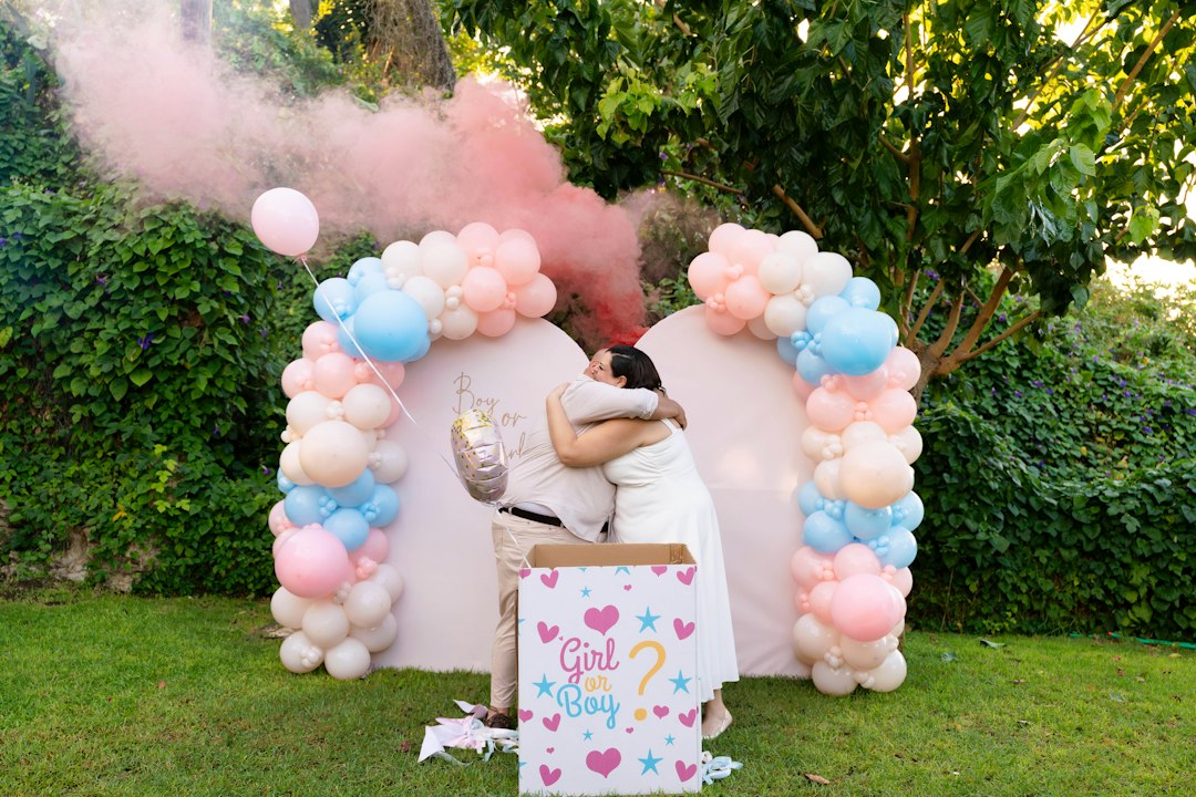 Two adults hugging in front of a pink and blue balloon arch with pink smoke