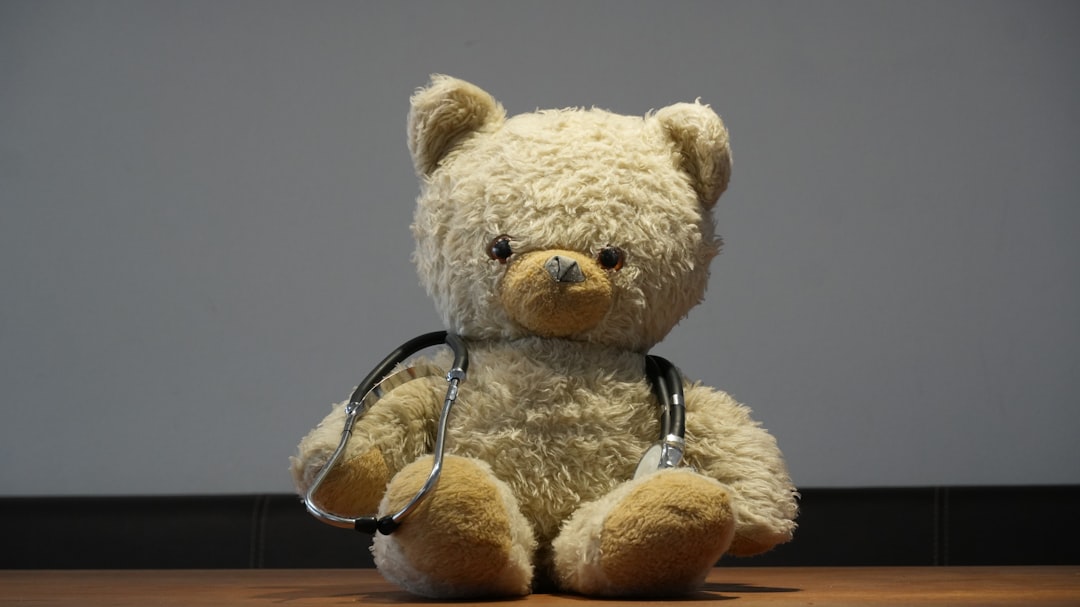 A teddy bear wearing a stethoscope sits on floor.