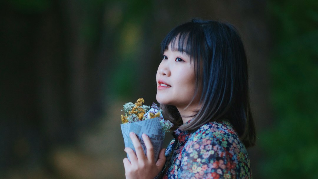 girl in blue and red floral shirt holding white flower
