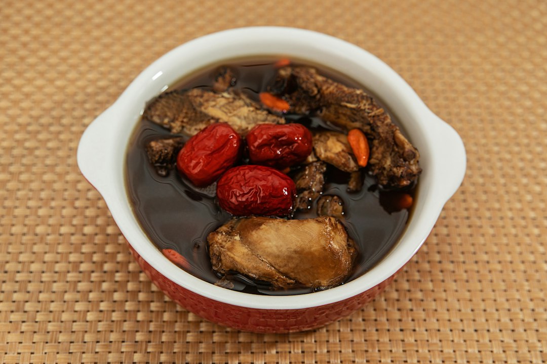 A bowl of dark herbal soup with chicken, red dates, and goji berries