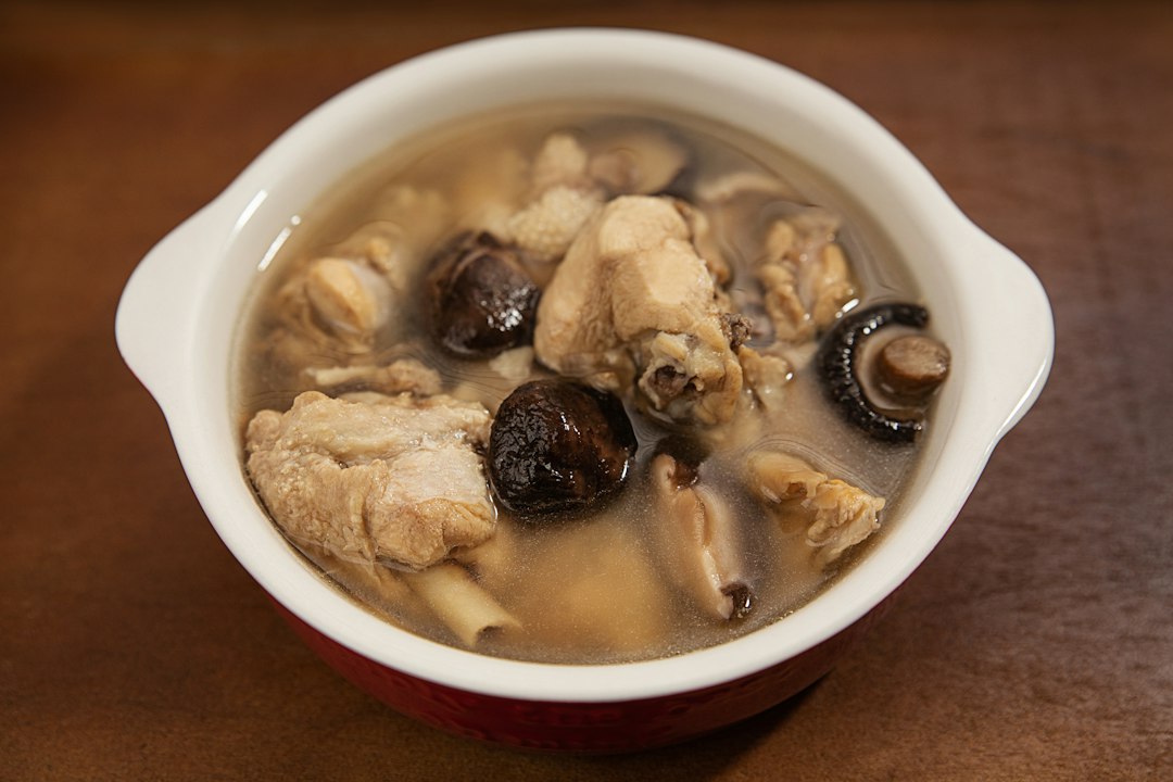 A bowl of chicken and shiitake mushroom soup on a wooden surface