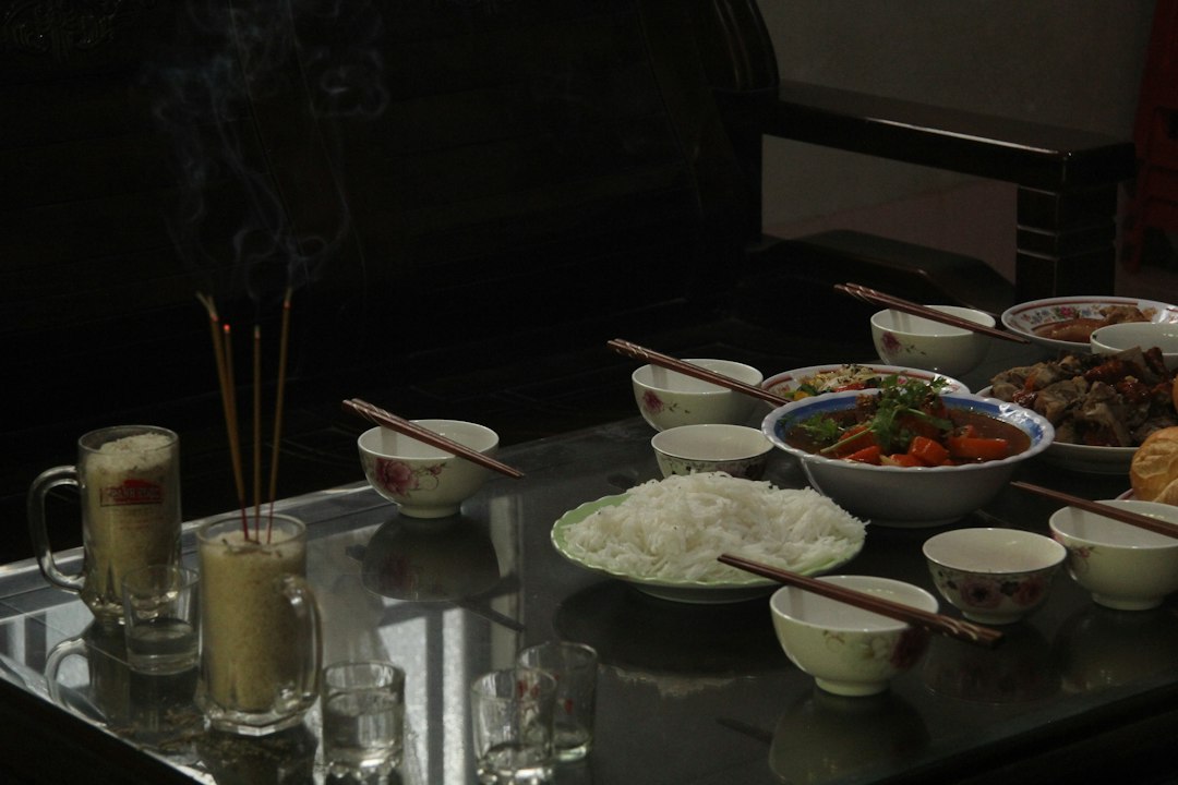Incense sticks burning in a glass of rice beside a meal on a table