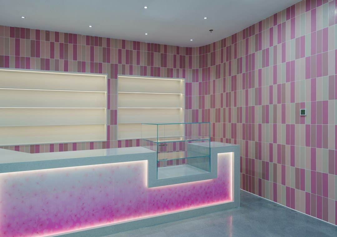 A retail counter with a glass display case against pink and beige tiled walls