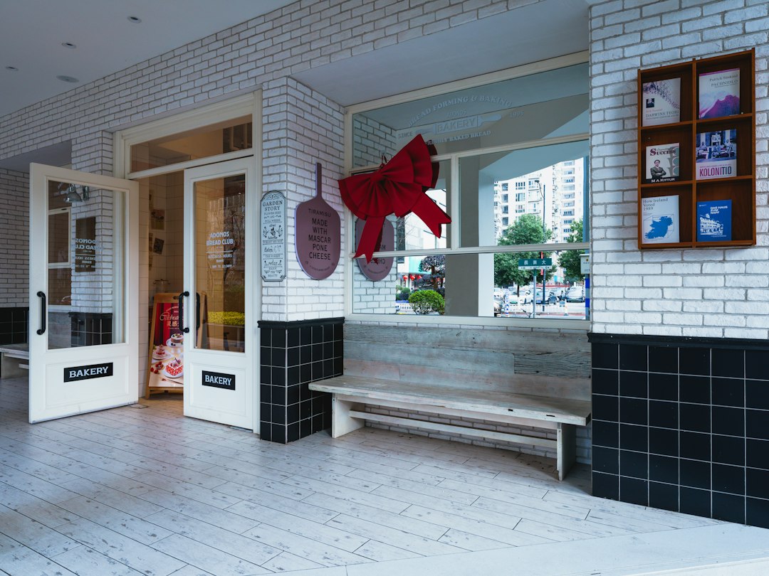 White brick storefront with black tiles, wooden bench, red bow