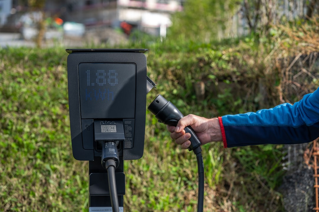 Hand holding electric car charger near charging station.
