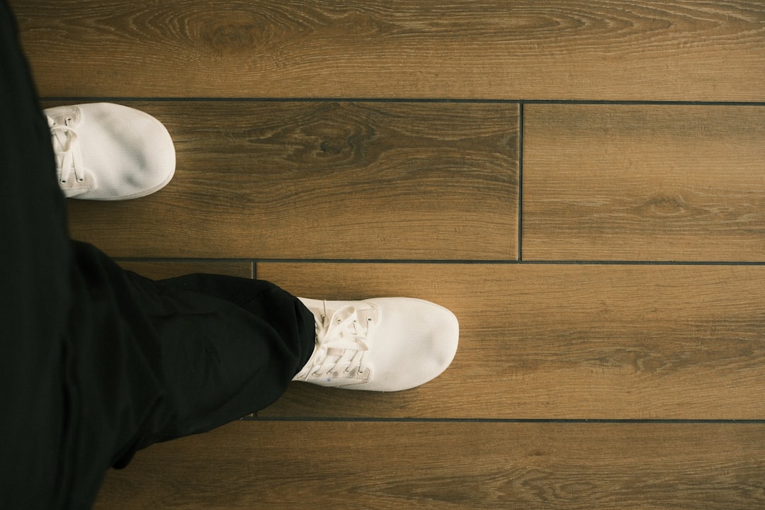 A person wearing white sneakers walks on a wooden floor.