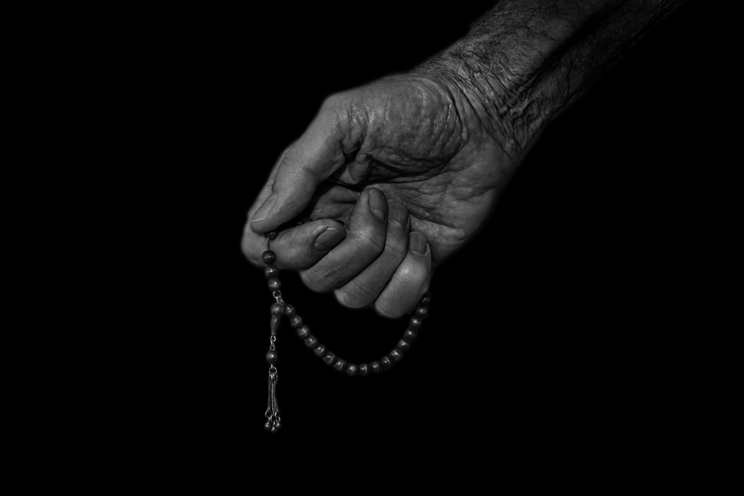 A hand holds a rosary against a black background.