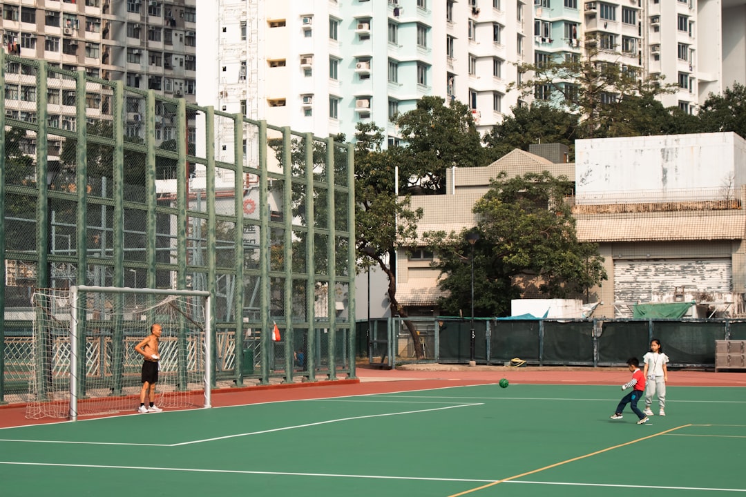 People playing soccer on a green field with buildings behind.