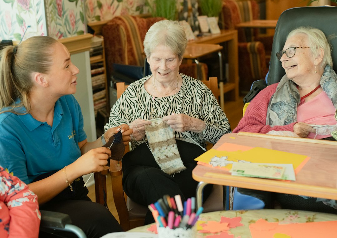 Caregiver assists two elderly women knitting