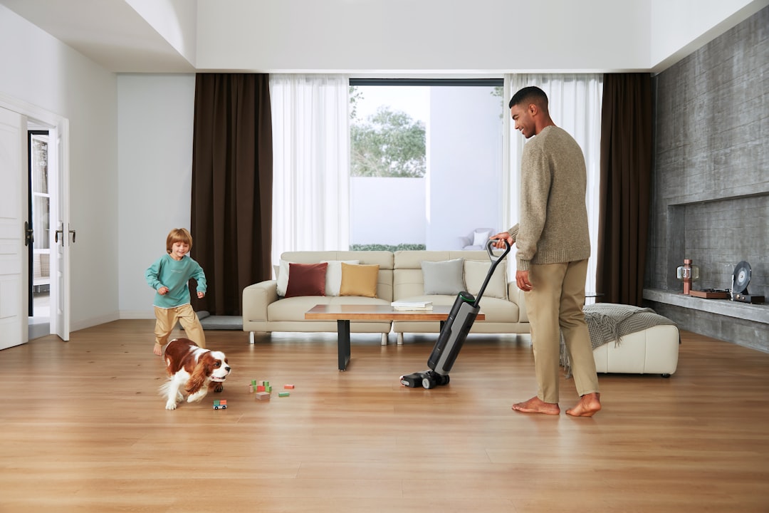 Man vacuums floor while child and dog play