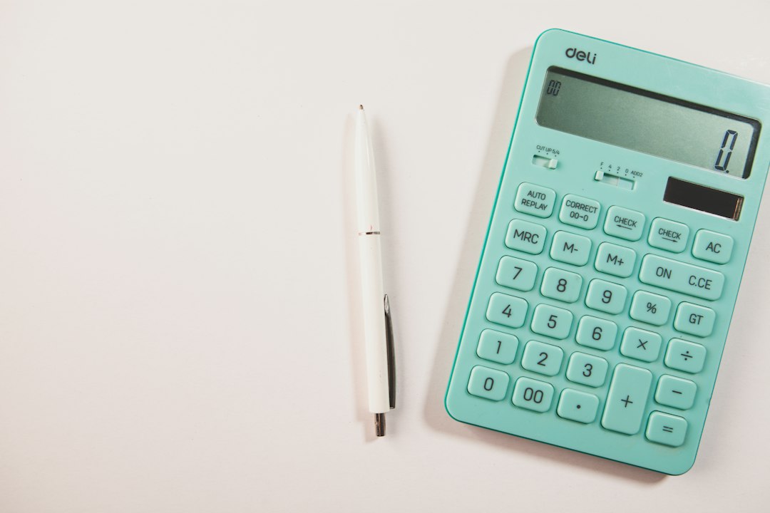 A teal calculator and white pen on a white surface