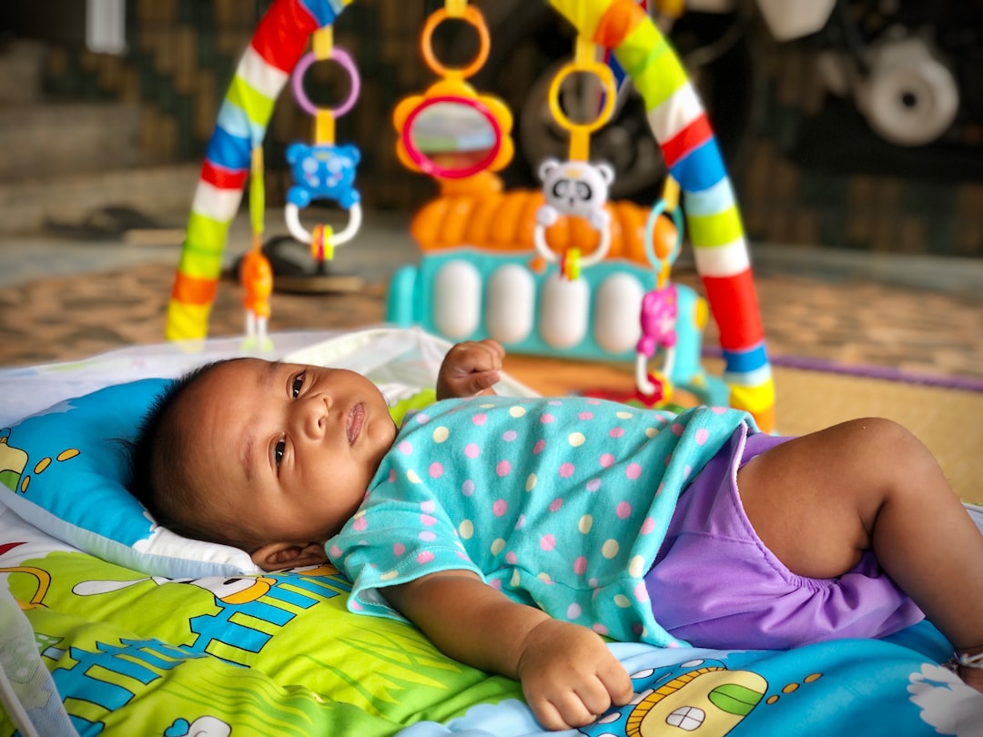 baby in pink and white tank top lying on green and blue mat
