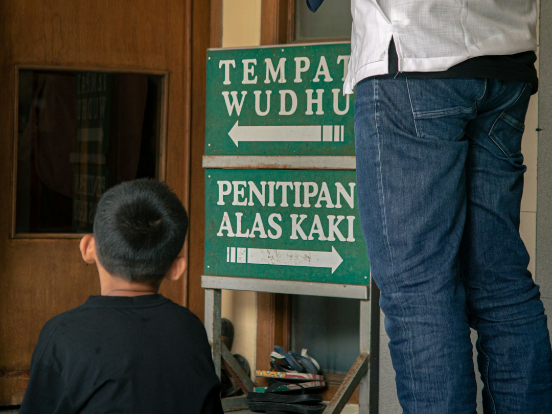 Two people stand near signs for ablution and shoe storage