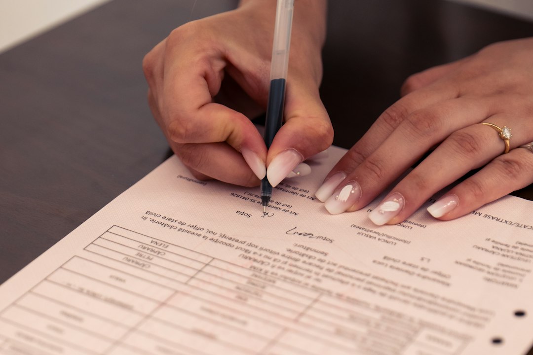 A person signing a document with a black pen on a dark table