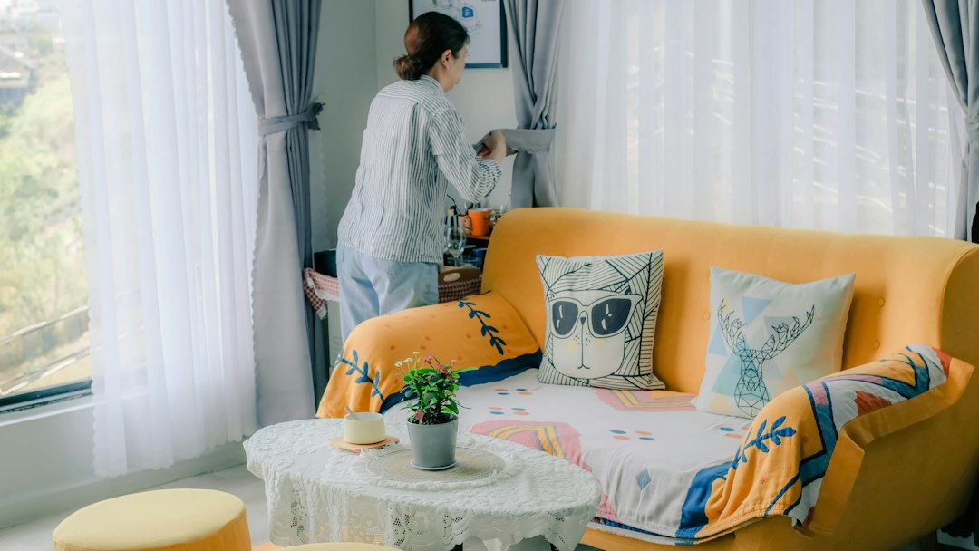 A woman adjusting curtains in a sunlit living room with a yellow sofa