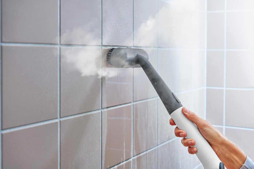 Steam cleaner sanitizing tiled wall in bathroom.