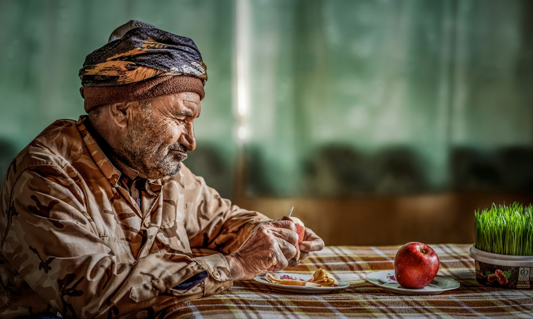 An elderly man eating at a table with an apple