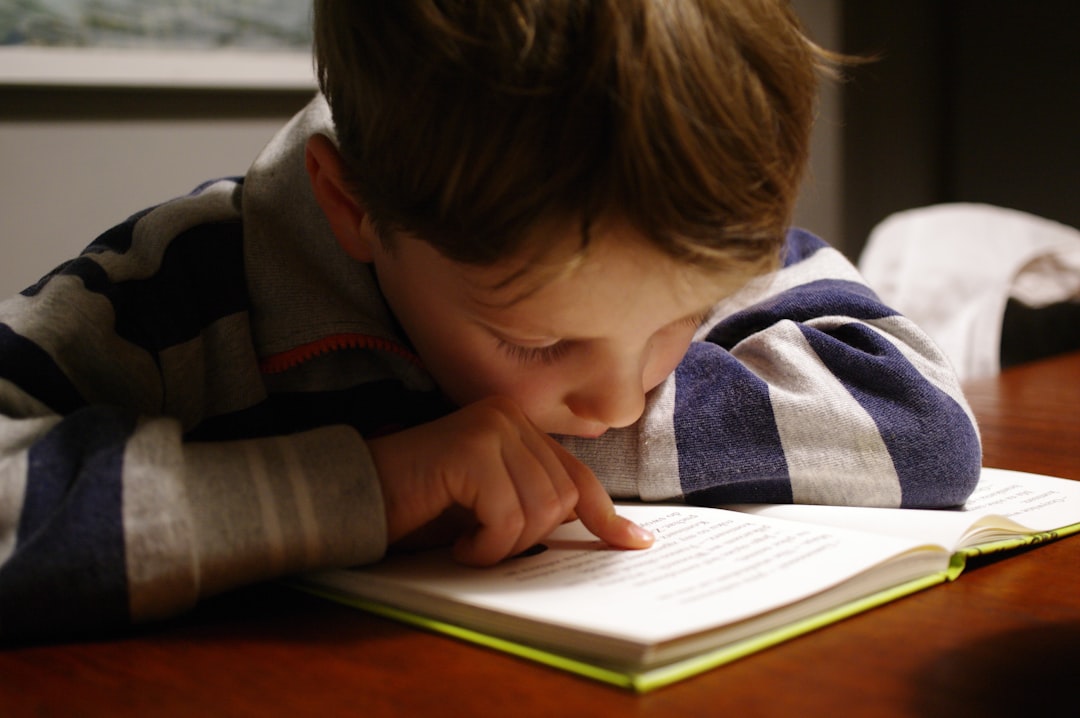 A child in a striped shirt reading a book at a wooden table