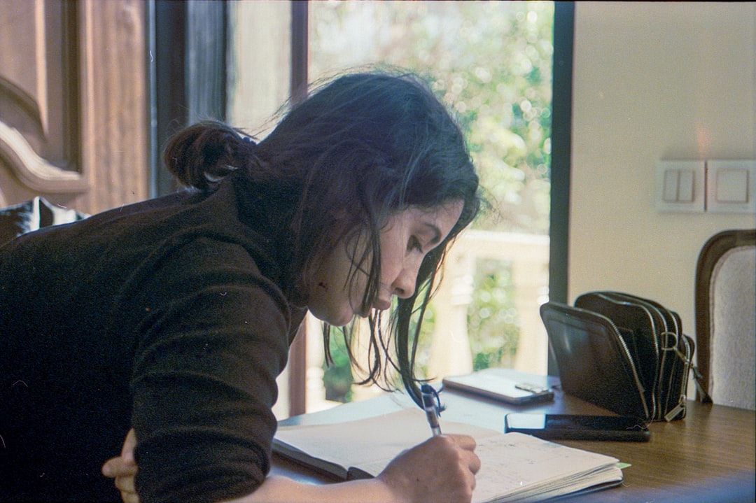 A woman writes in a notebook at a table.