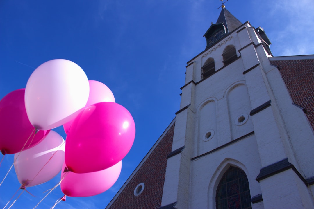 Pink balloons float against a church and sky