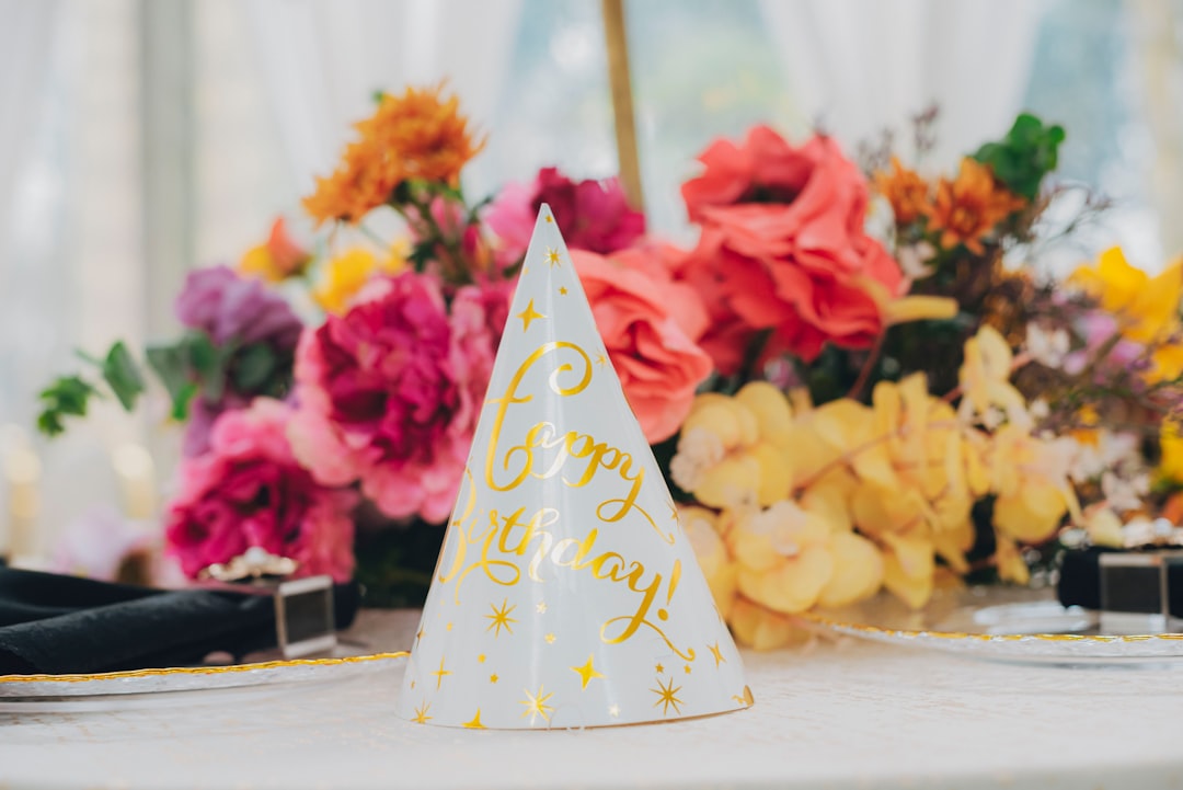 Party hat with gold stars sits before flowers.