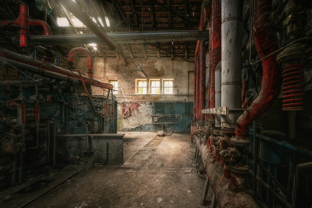 An abandoned industrial room with red pipes and a shovel on a concrete floor