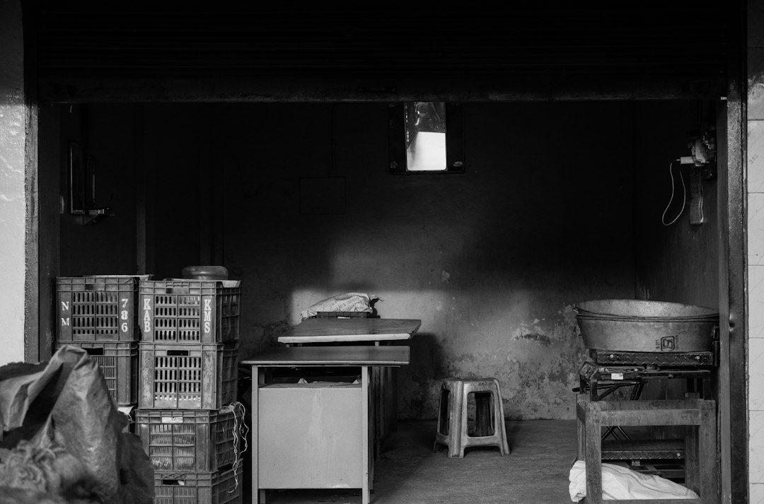 A stack of plastic crates beside tables and a stool in a dim room