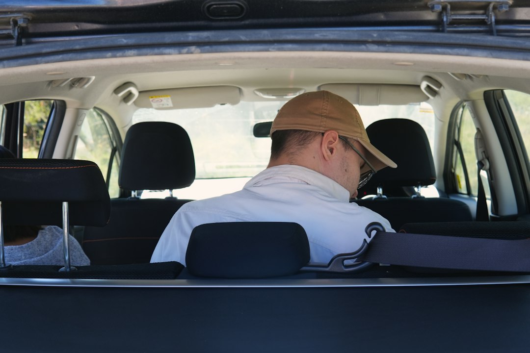 A person in a tan baseball cap sitting in the back seat of a car
