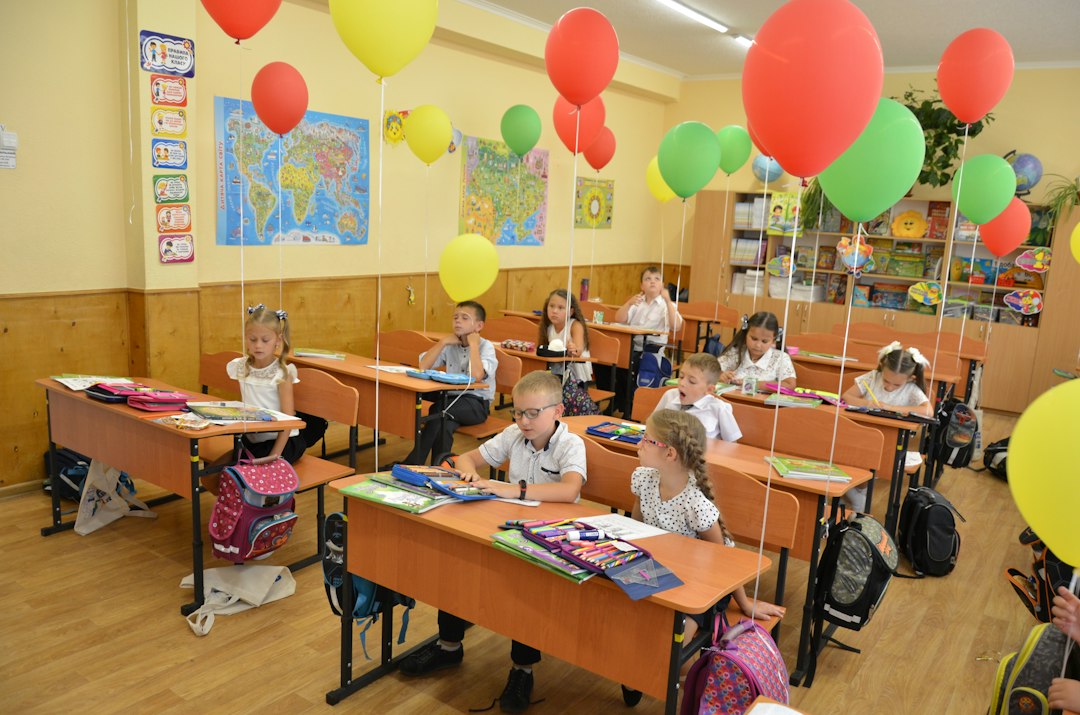 Children sitting at desks in a classroom decorated with balloons