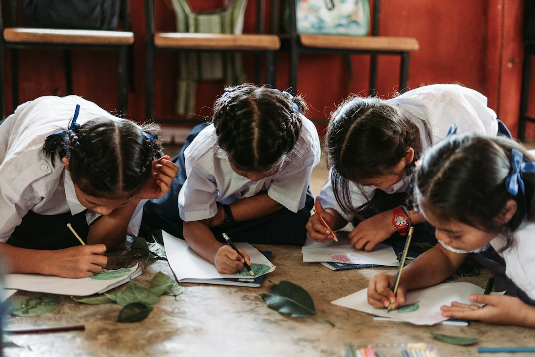 Four children in white school uniforms drawing on paper while sitting on the floor