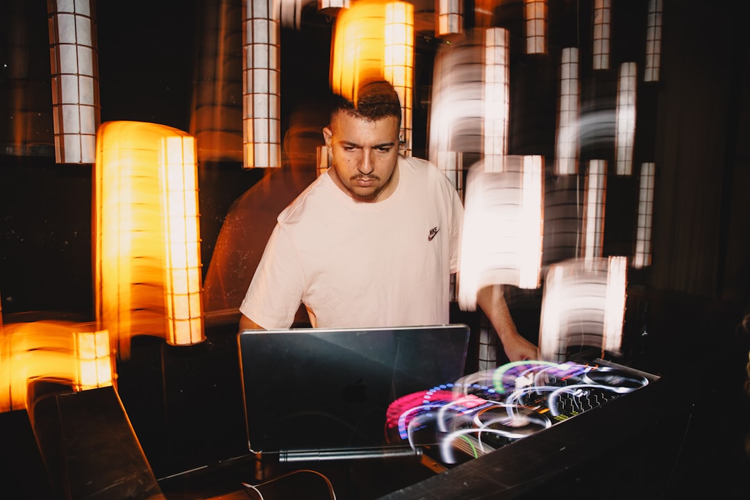 Dj performing with laptop and equipment at night.