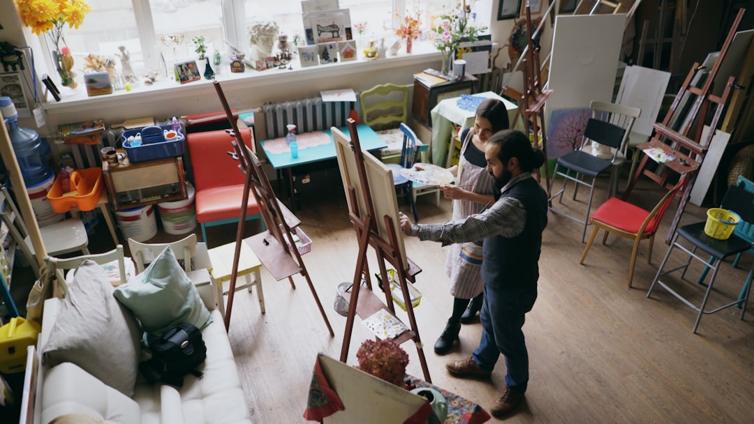 Two people painting in a bright, cluttered art studio.