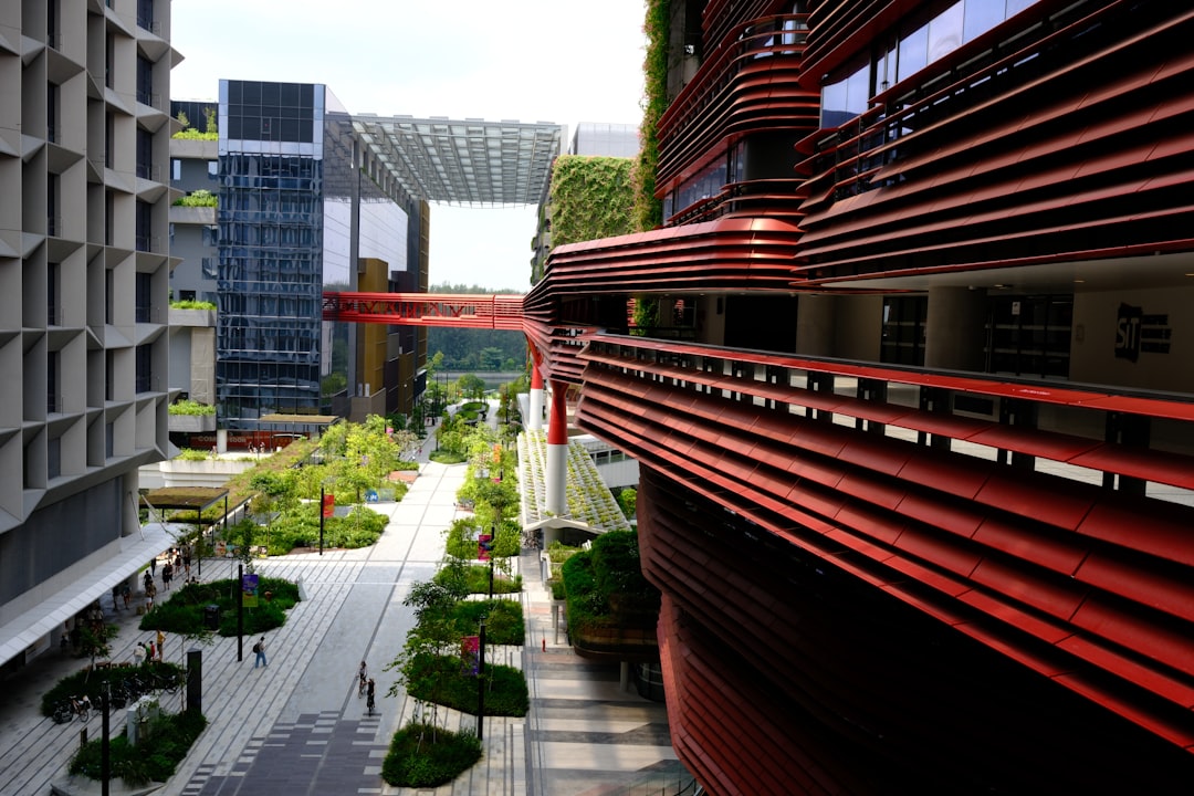Modern red and grey buildings with a green urban walkway.