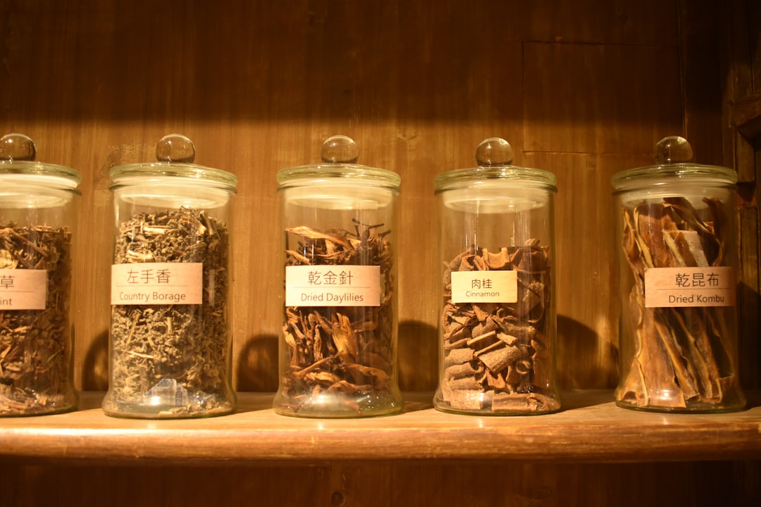Glass jars filled with dried herbs on wooden shelf.