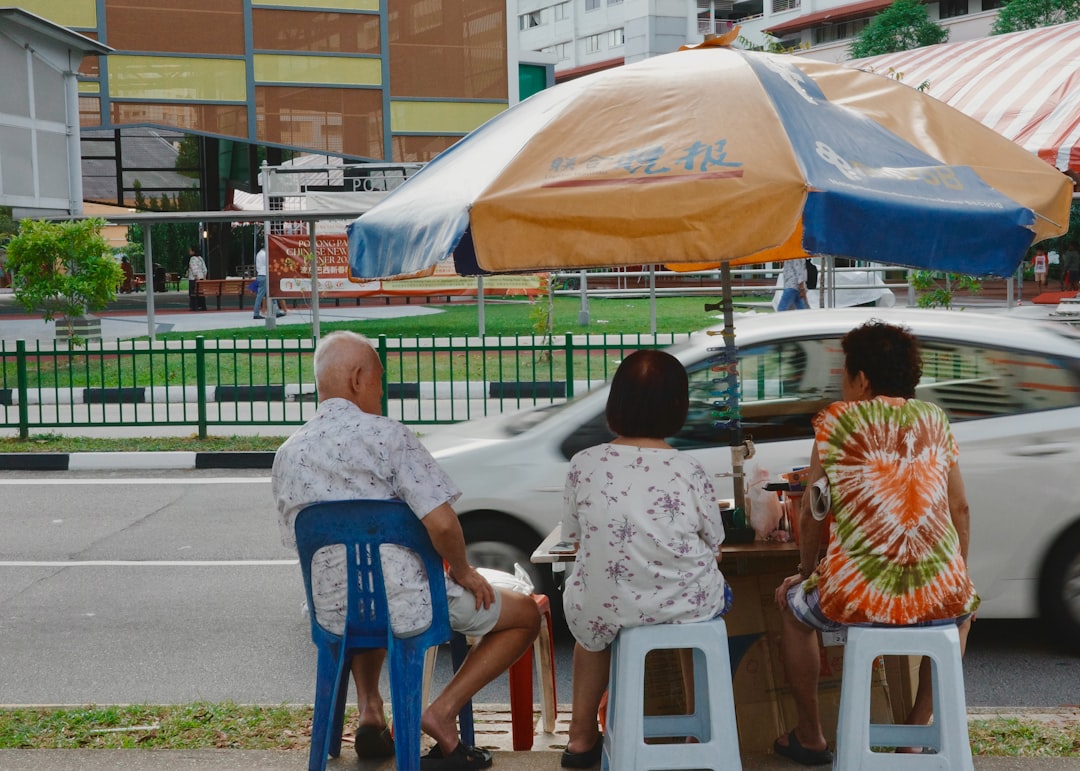 Three people sitting under an umbrella by the road