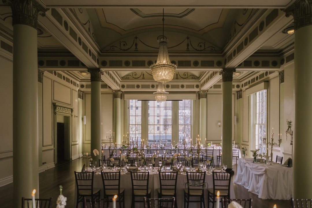 Elegant ballroom with long tables, chandeliers, and tall columns.