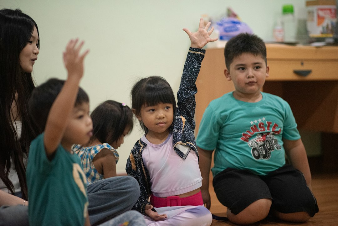 A group of children sitting on a floor with hands raised in a classroom