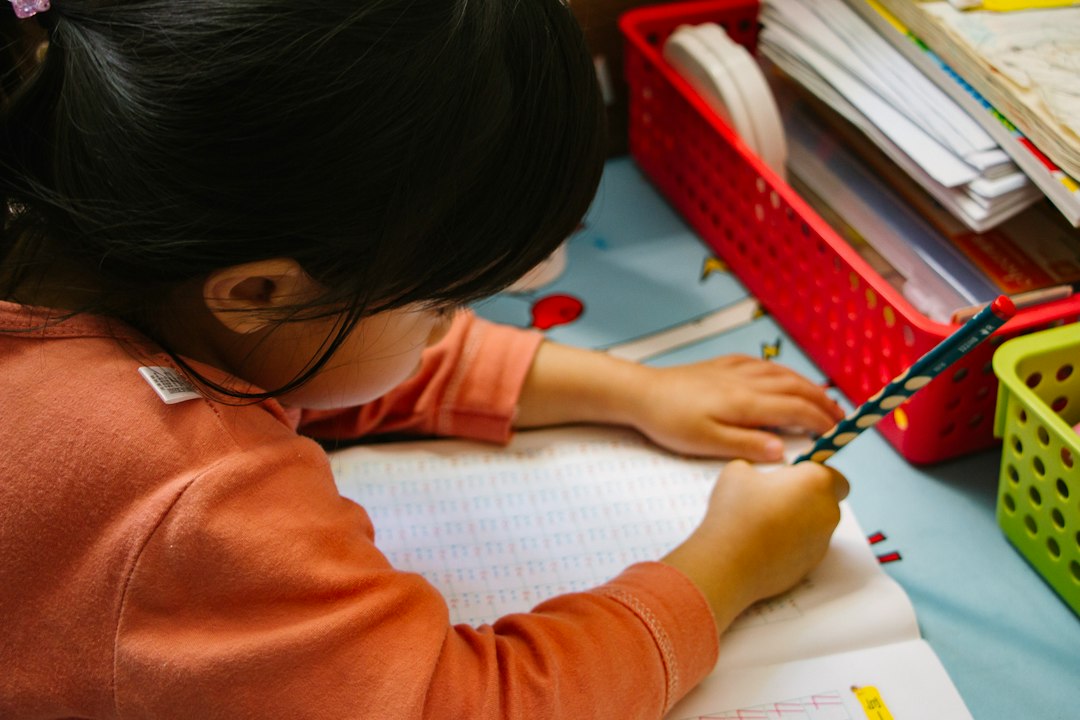 girl in orange long sleeve shirt writing on white paper