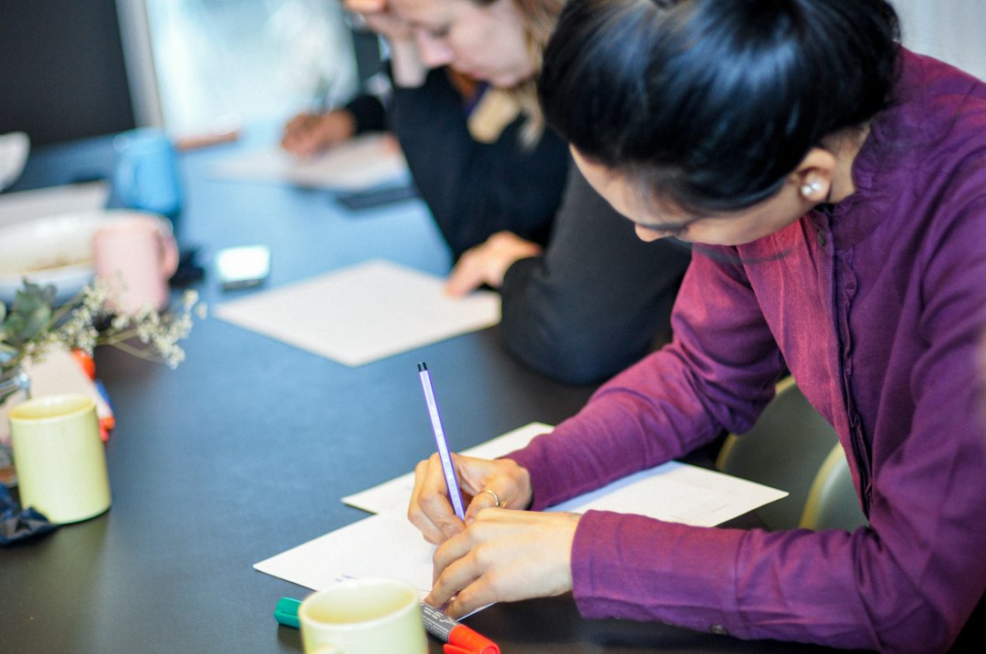 a woman sitting at a table writing on a piece of paper